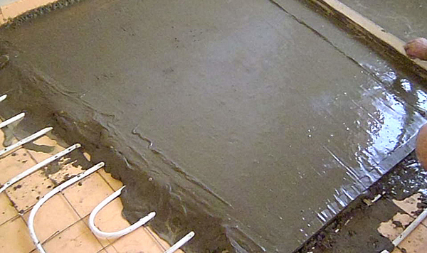 На фото – с помощью правила доводим раствор стяжки пола до уровня маяков